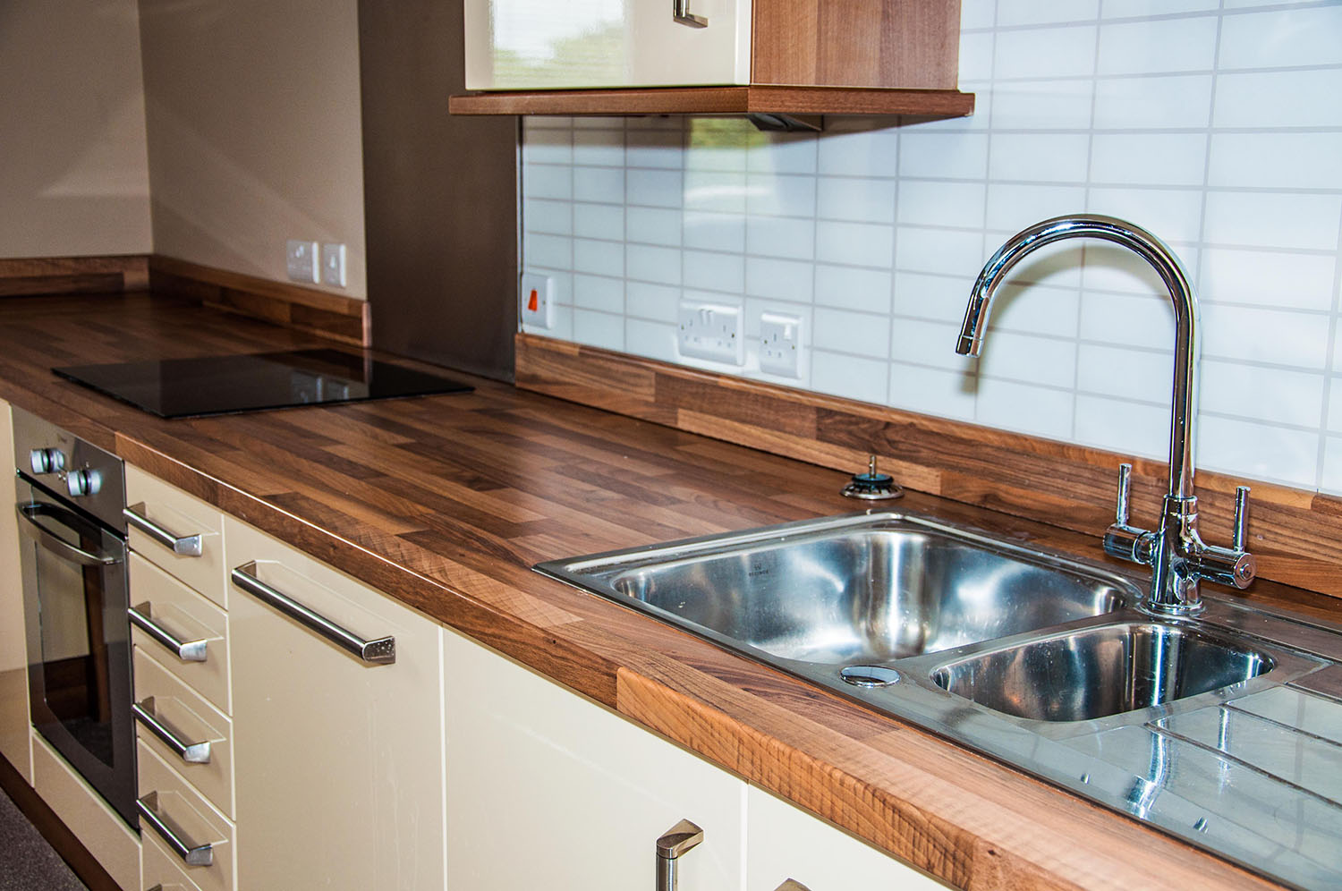 Kitchen wooden countertop with beige cupboards and a stainless steel sink and tap