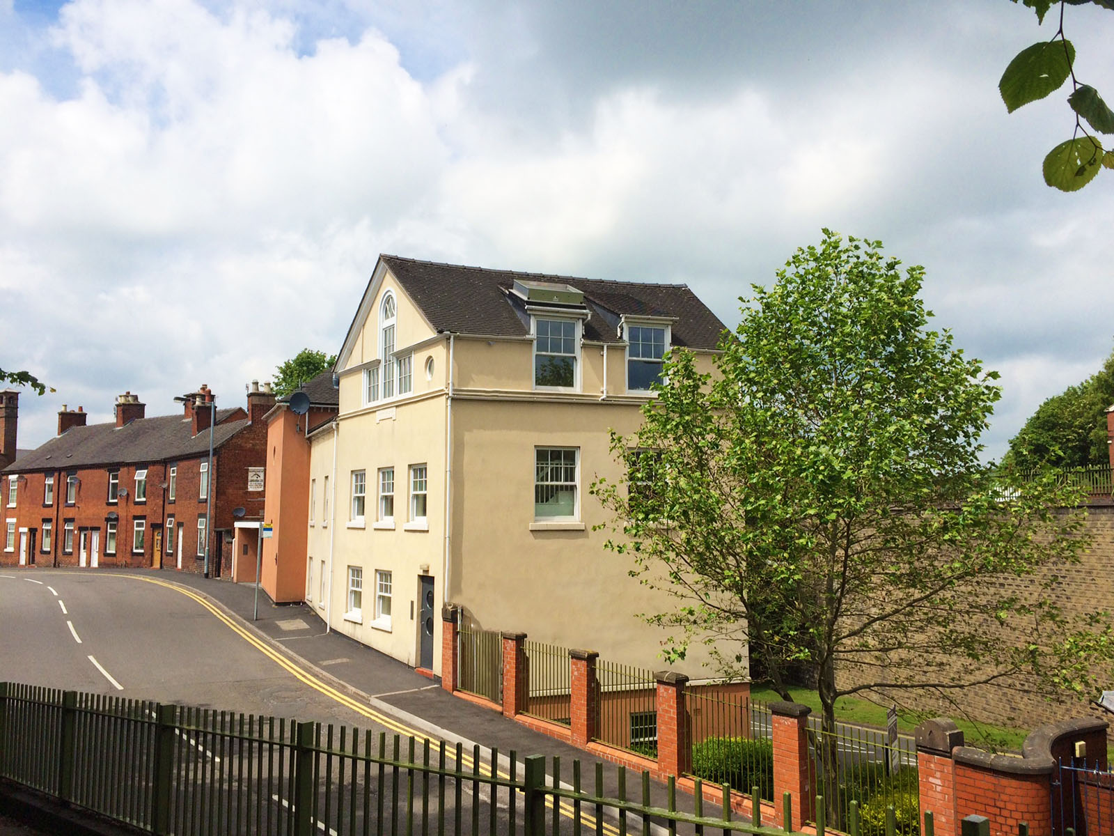 External view of a 3 storey yellow house with a large tree in the garden area to the right