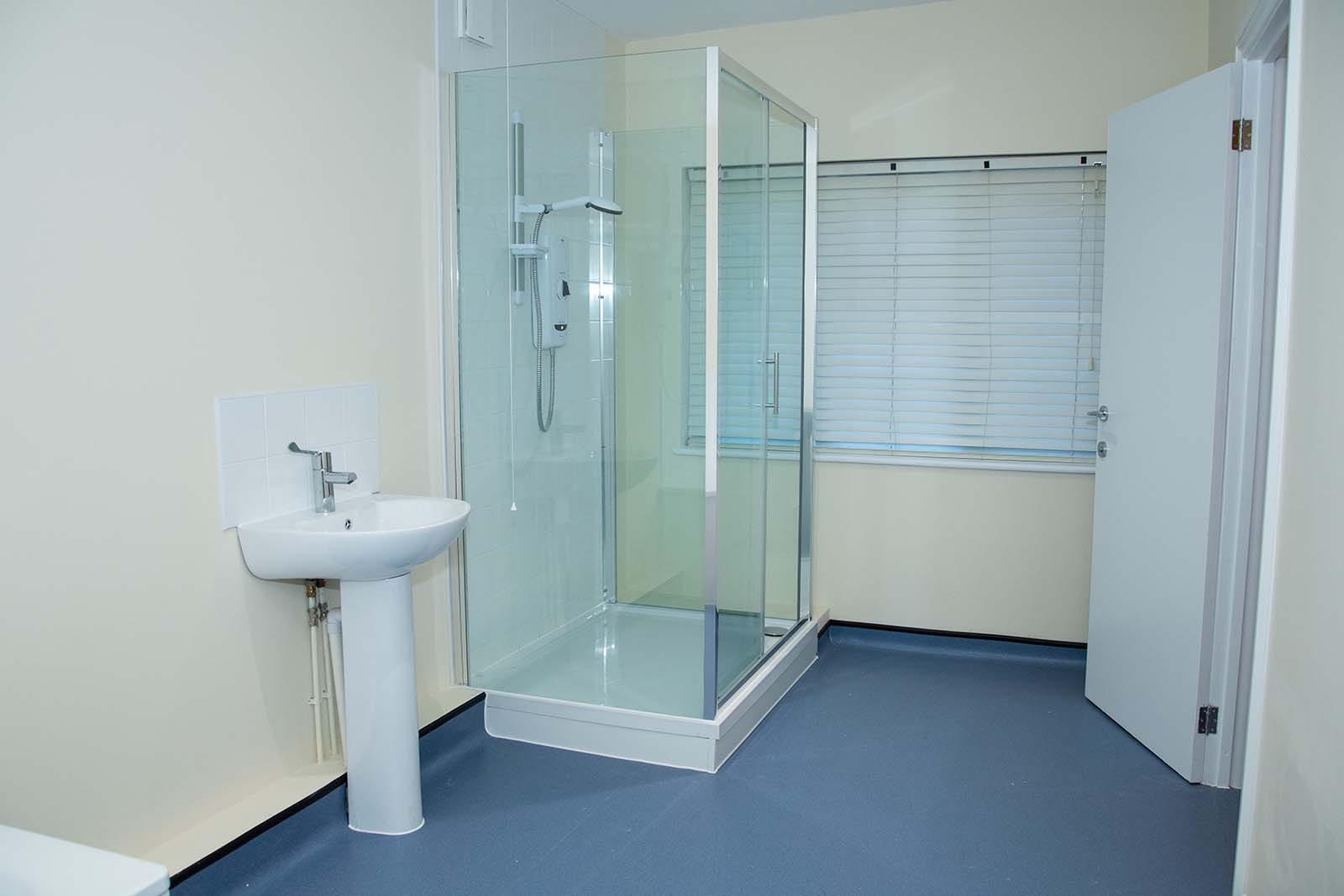A bathroom with a blue floor, a glass shower and a sink and one window