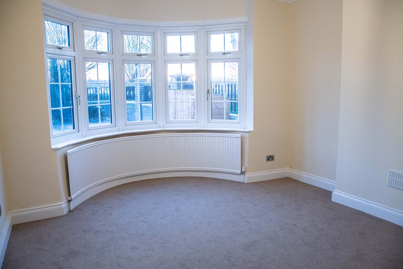 an empty living room with gray carpet and a large bay window